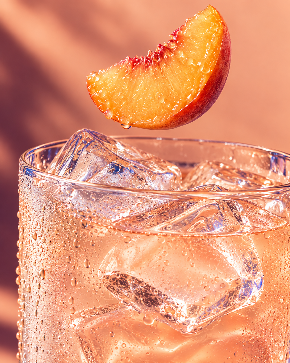 An appetizing peach drink with clear ice and a peach wedge